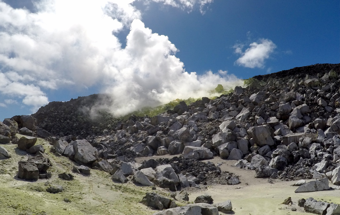 Steam rising out of volcanic rock showing green sediment