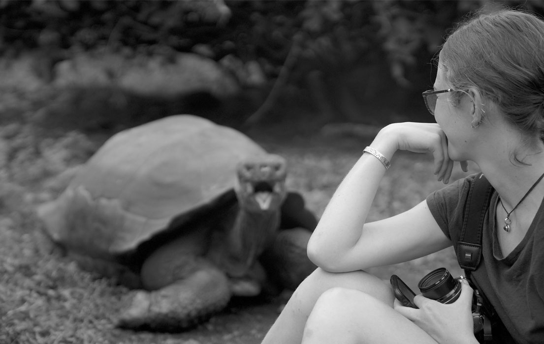Woman observing giant tortoise closely in black and white.